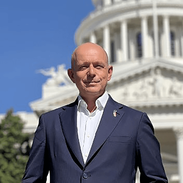 Headshot of Steve Hilton standing in front of the Capitol building wearing a dark blue suit